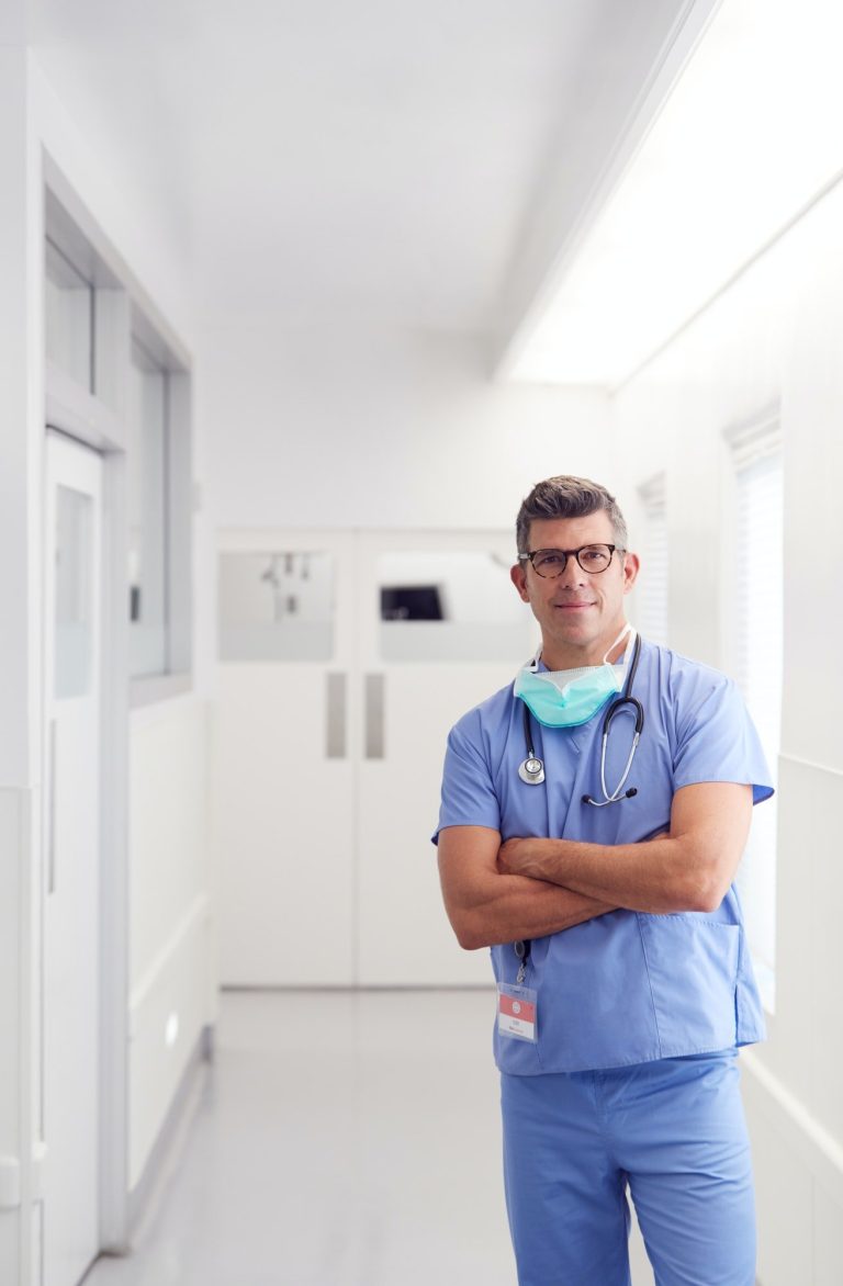 portrait of mature male doctor wearing scrubs standing in hospital corridor.jpg
